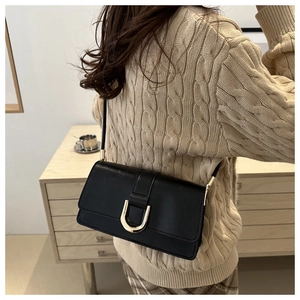 Sac bandoulière en cuir noir avec boucle dorée en U sur un pull en maille beige