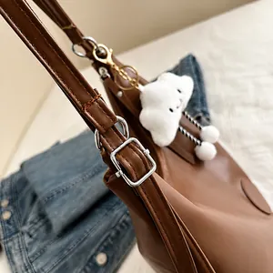 Detailed view of brown leather bag strap with silver metal buckle and cloud plush charm