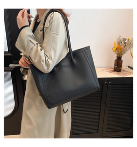 Borsa tote in pelle nera indossata da modella con cappotto beige stile ufficio