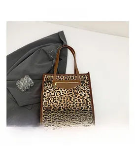 Detail of leopard print tote bag featuring a front zipper pocket and brown leather handles