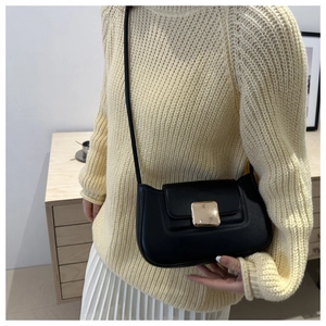 Detail einer schicken schwarzen Schultertasche mit goldener Metallschnalle auf Strickpullover