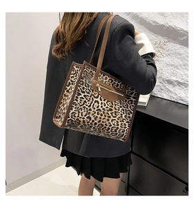 Detail of leopard print tote bag with brown leather trim worn by a model in a grey blazer