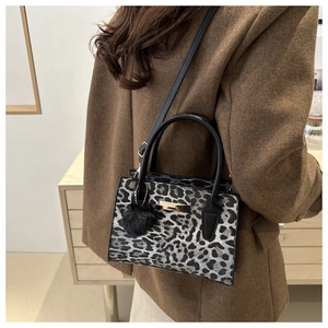 Détail du sac à main léopard avec poignées noires et un charmant pompon en peluche noir