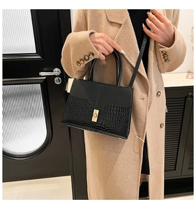 Gros plan d'un sac à bandoulière noir avec motif crocodile et fermoir en métal doré