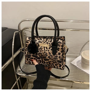 Detail showing leopard print texture, black leather handle and plush ball charm on a bag
