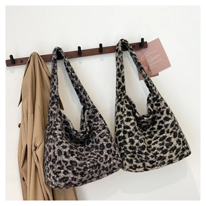 Plush leopard print tote bags in brown and grey hanging against a minimalist white wall