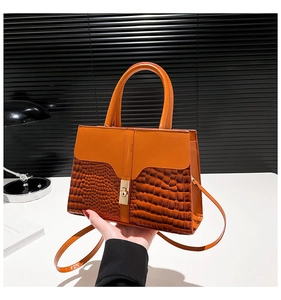 Detail of orange stone-patterned handbag featuring gold twist lock and smooth leather panel