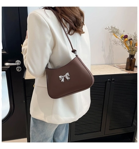 Sac porté épaule en cuir marron avec nœud argenté, porté par un mannequin en blazer blanc