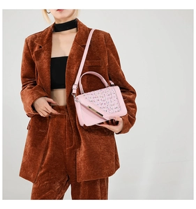Détail d'un sac bandoulière en tweed rose avec garniture dorée porté sur un habit marron