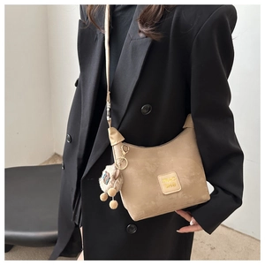 Fashionable khaki suede crescent bag shown on model with adjustable strap and pompom charm