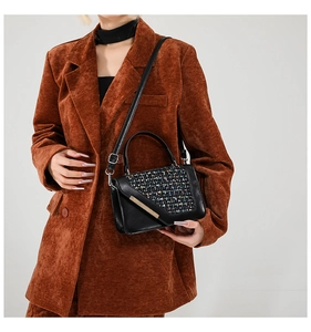 Détail du sac à main en tweed et cuir noir porté avec un blazer en velours côtelé orange