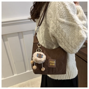 Detail of dark brown dumpling bag with pleated faux leather texture and plush ball charm