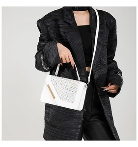 Gros plan d'un sac bandoulière blanc en tweed porté avec un blazer noir texturé