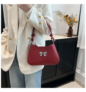 Sac rouge sous le bras avec nœud argenté porté sur une tenue avec blazer blanc chic