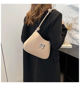 Détail du sac beige avec nœud argenté porté sur un blazer noir élégant pour femme