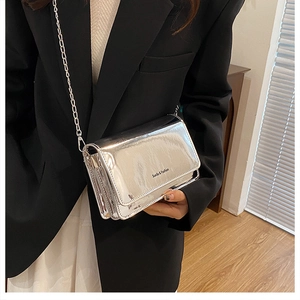 Detail van zilveren spiegel schoudertas met metalen ketting gedragen op een zwarte blazer
