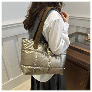 Détail du sac fourre-tout matelassé or champagne porté à l'épaule par un mannequin