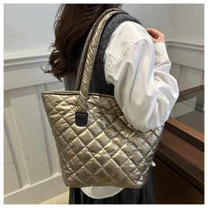 Detalle del bolso tote acolchado dorado con forma de trapecio y textura metálica al hombro