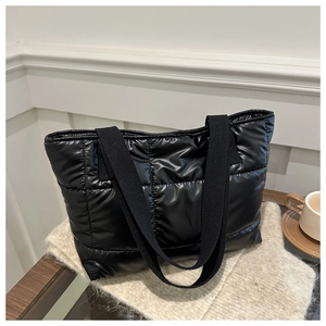 Détail d'un sac cabas noir matelassé sur tricot beige avec une tasse de café