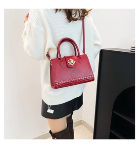 Detail of red faux leather handbag with crocodile pattern and golden flower buckle