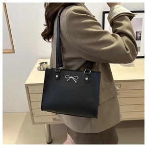 Detail of black tote bag featuring a silver bow metal buckle and thin shoulder straps