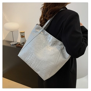 Detail van grote zilveren tote bag met krokodillenreliëf over de schouder gedragen voor werk