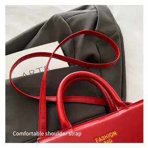 Dettaglio borsa in pelle rossa con scritta moda, manici robusti e tracolla sottile