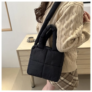 Detalle de bolso acolchado negro con textura suave de rejilla y correa ancha al hombro