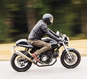 Dynamic side view of a rider wearing protective black leather jacket and riding pants on a motorcycle