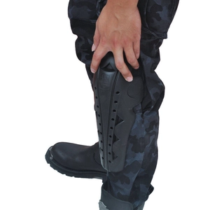 Detail of black motorcycle shin guards with ventilation holes on camouflage pants