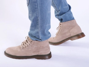 Detail of tan suede motorcycle boots with yellow stitching and durable rubber sole