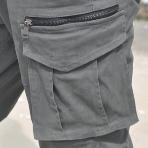 Detail of grey cargo pants featuring a vertical metal zipper and a flap utility pocket