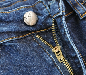 Macro detail of YKK zipper and branded metal button on blue motorcycle jeans