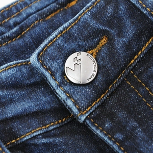 Detail of matte silver button with engraved logo on deep blue denim motorcycle jeans