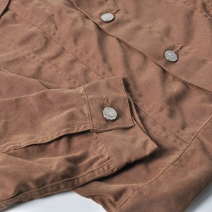 Detailed close-up of heavy brown canvas motorcycle jacket with metallic V-embossed buttons