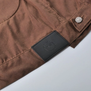 Detail of a brown waxed motorcycle jacket featuring a leather brand patch and metal button