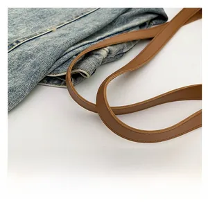Detail of blue denim tote bag featuring premium brown leather shoulder strap and stitching