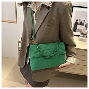 Sac enveloppe matelassé vert avec chaîne décorative porté sur un blazer élégant
