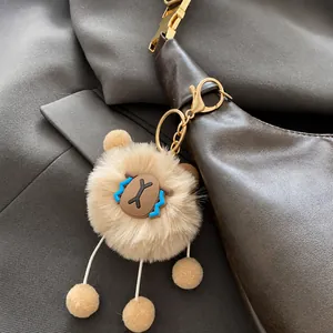 Close-up of a cute light brown plush bear charm with gold metal clasp on a leather bag