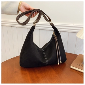 Detail van zwarte suède hobo tas met contrasterende stiksels en leren riem op houten tafel
