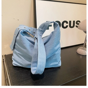 Détail du sac cabas en denim bleu clair avec œillets métalliques et bandoulière large