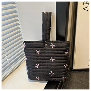Dettaglio del fiocco rosa ricamato su borsa trapuntata nera con chiusura a scatto
