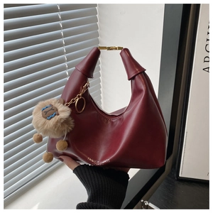Close-up of burgundy leather handbag with golden metal buckle and brown plush charm