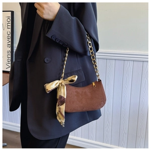 Primer plano de bolso sobaquero de ante marrón con cadena dorada y pañuelo decorativo