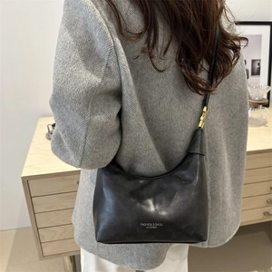 Chic black crescent leather shoulder bag with gold hardware and logo on grey coat