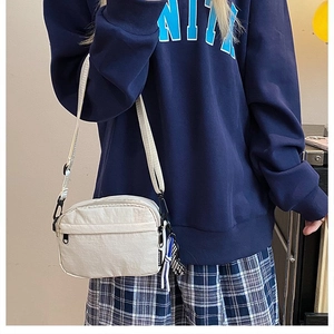 Dettaglio di una borsa a tracolla in nylon bianco con tracolla regolabile e ciondolo nastro