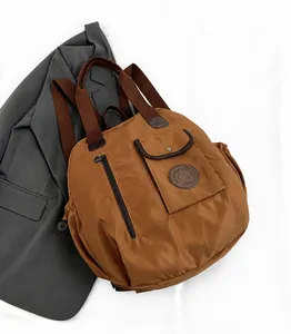 Dettaglio dello zaino in nylon marrone caffè con cerniera verticale e logo in pelle su letto