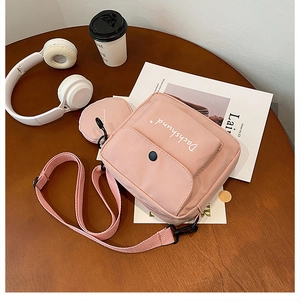 Pink canvas crossbody bag detail showing small coin purse and adjustable strap on wood desk