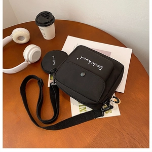 Detailed view of a black canvas crossbody bag with a round coin purse on a wooden table