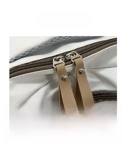 Close-up of dual brown zippers with stylish faux leather pull tabs on a beige fabric backpack